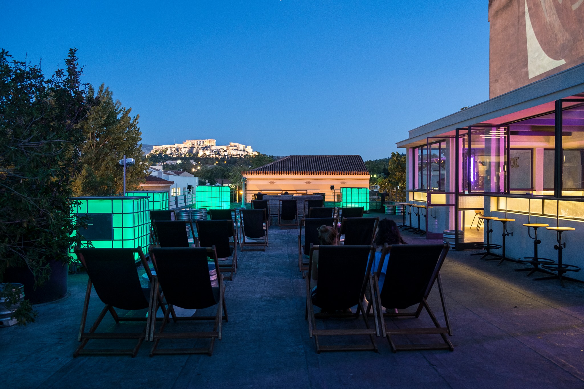 deck chairs lined on the terrace of rooftop bar BIOS in Athens, with a temple in the background 